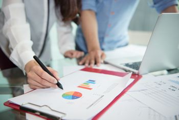 Two auditors reviewing a laptop and color charts printed on paper